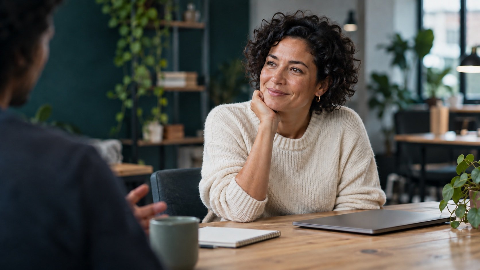 A woman listening thoughtfully to a colleague at a worktable